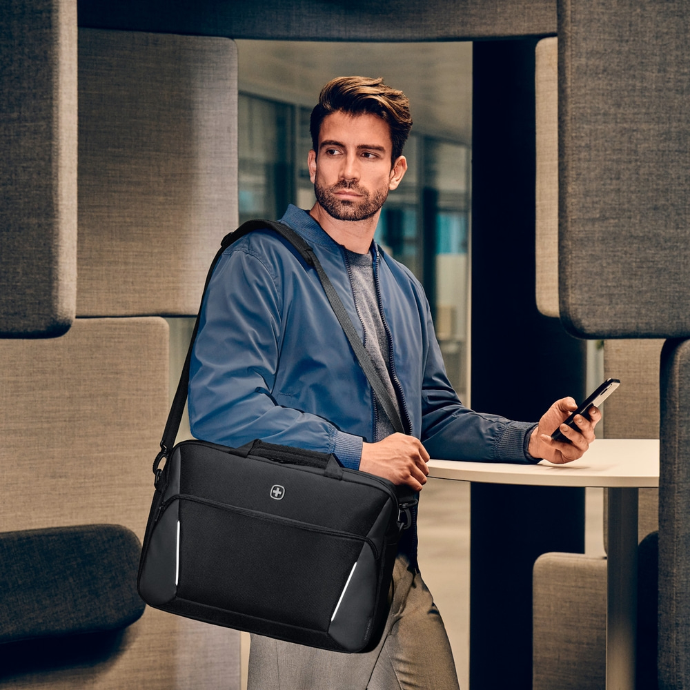 Man with black bag and phone in a modern office setting, looking away