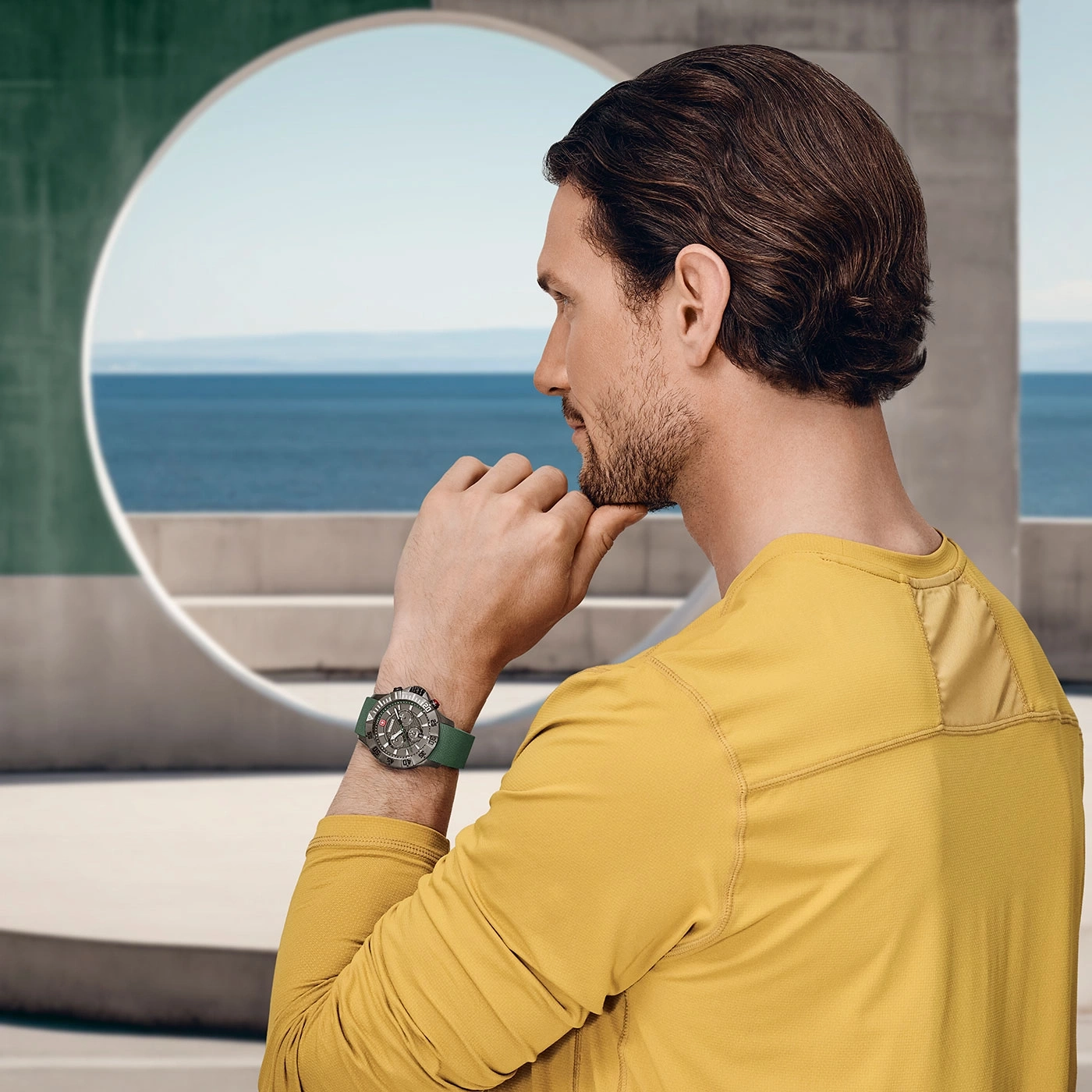 Mann mit Uhr, der über das Meer in einem gelben Hemd nachdenkt.