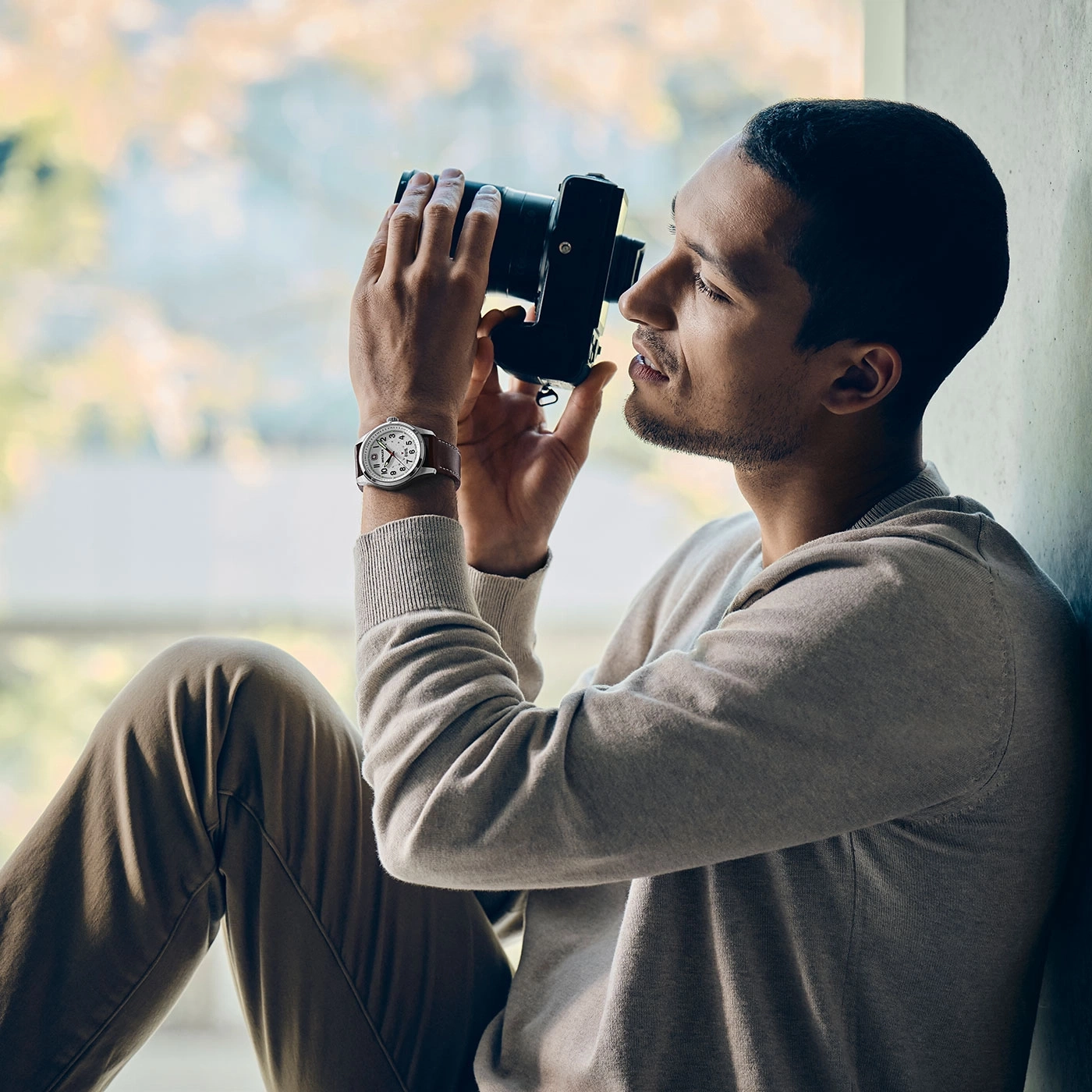 Ein Mann sitzt und fotografiert mit einer Kamera, die eine Uhr trägt.