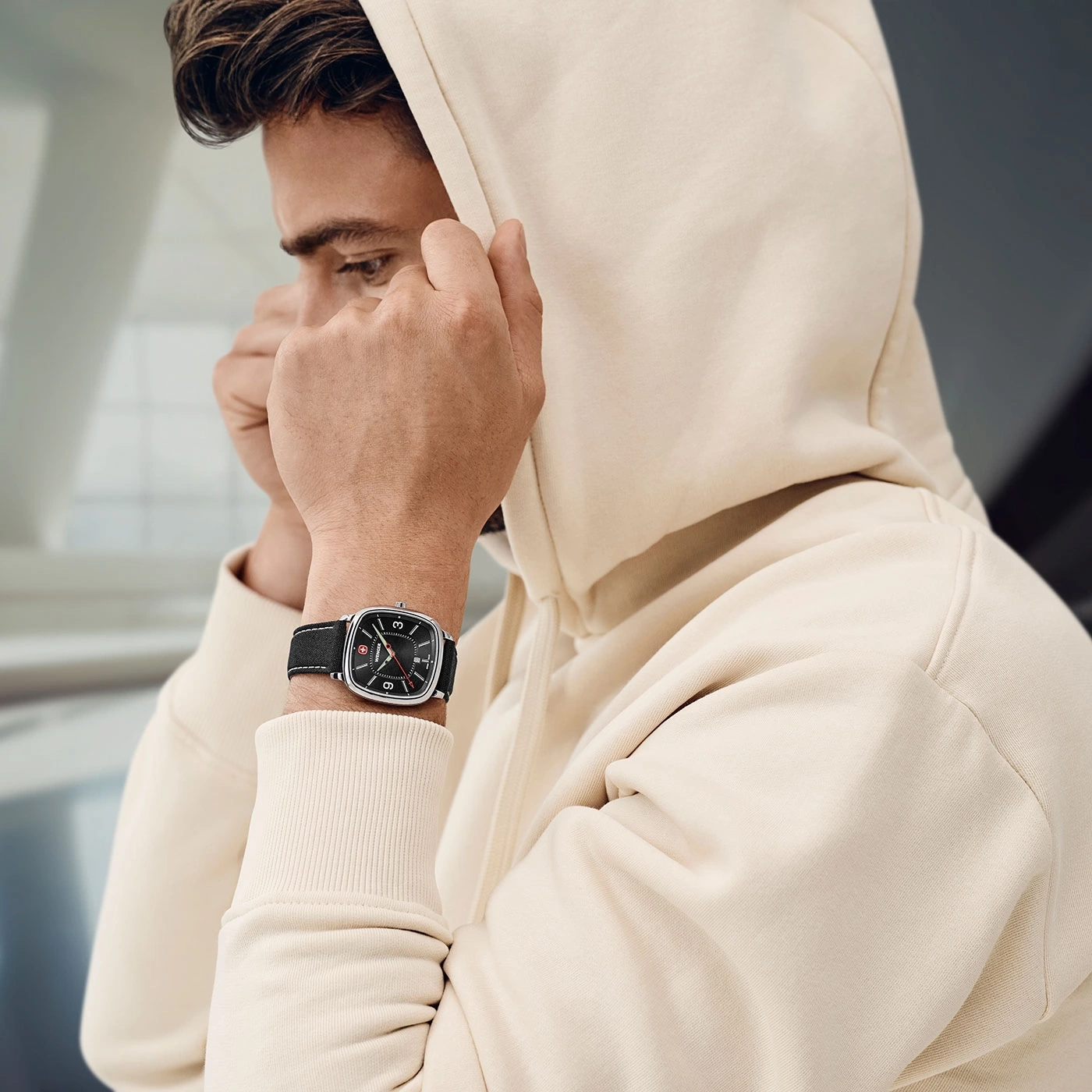 Man in hoodie with watch pulling hood over head, looking down, close up.