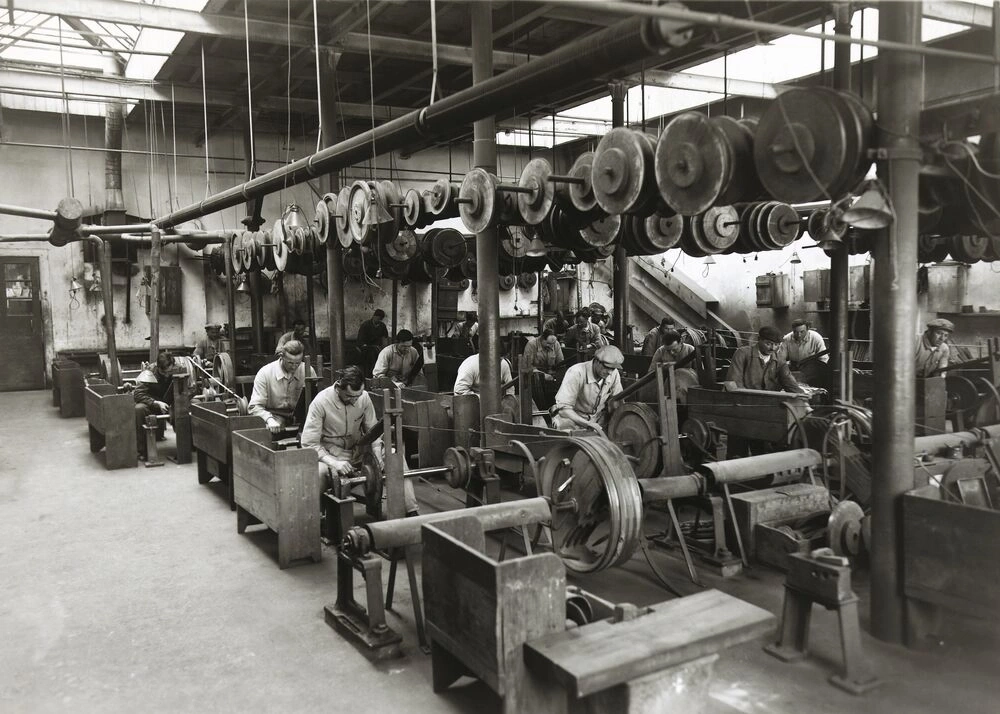 Workers in a factory with machines and belt drives.