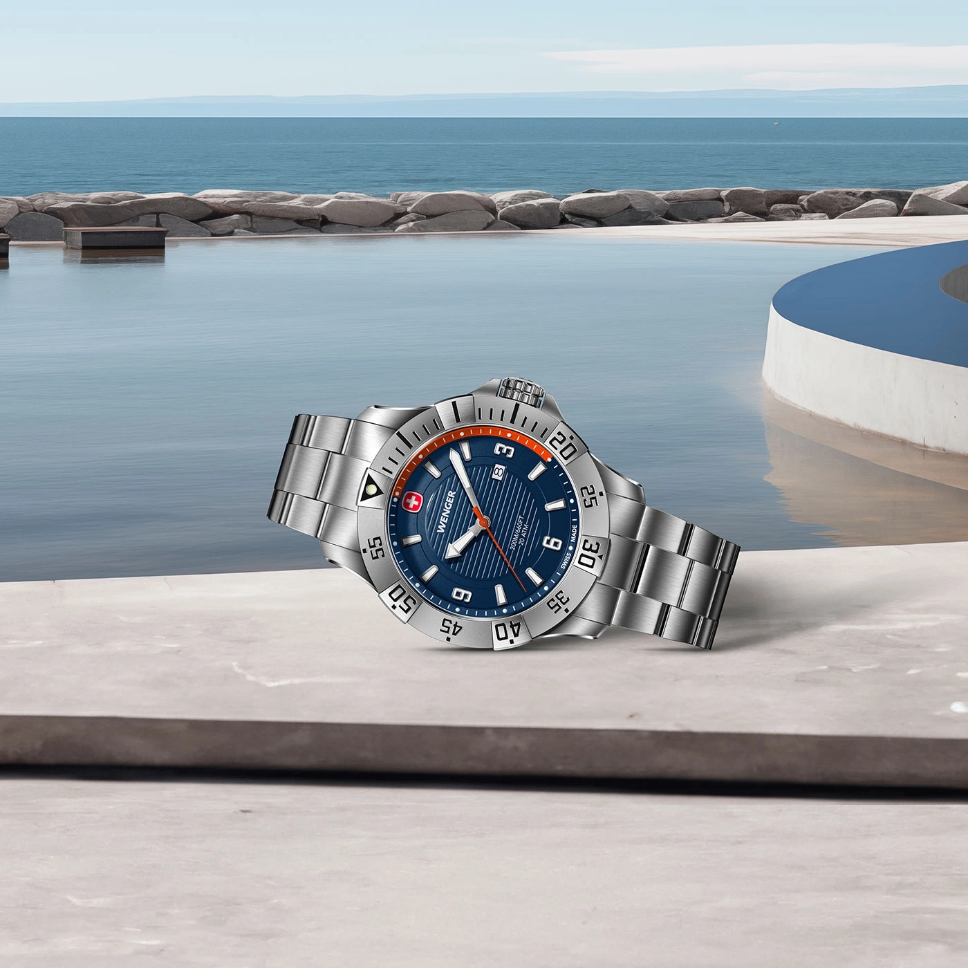 Watch by the pool. Blue watch with silver bracelet. Water and sky in the background.