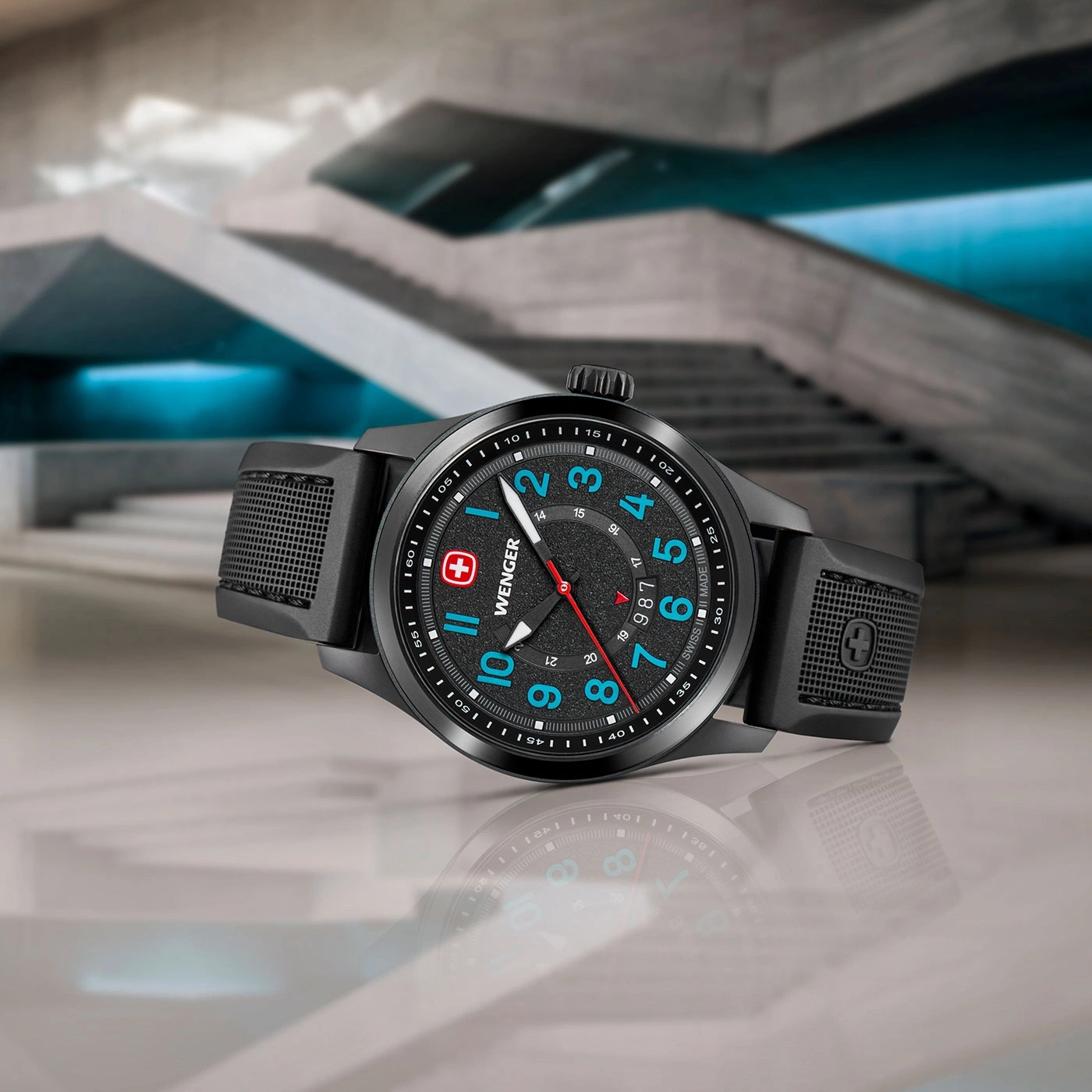 Black Wenger watch with blue and red accents, set on a reflective surface.