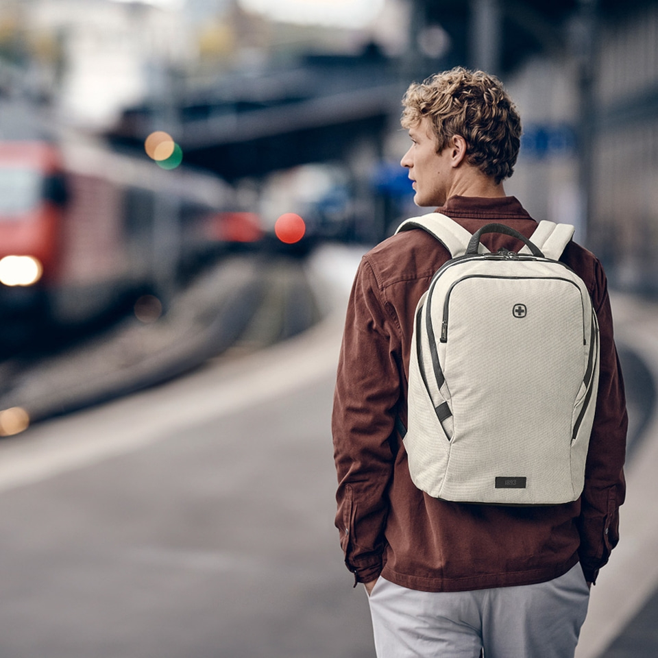 Man with backpack waiting at train station. Cityscape in the background. Travel concept.