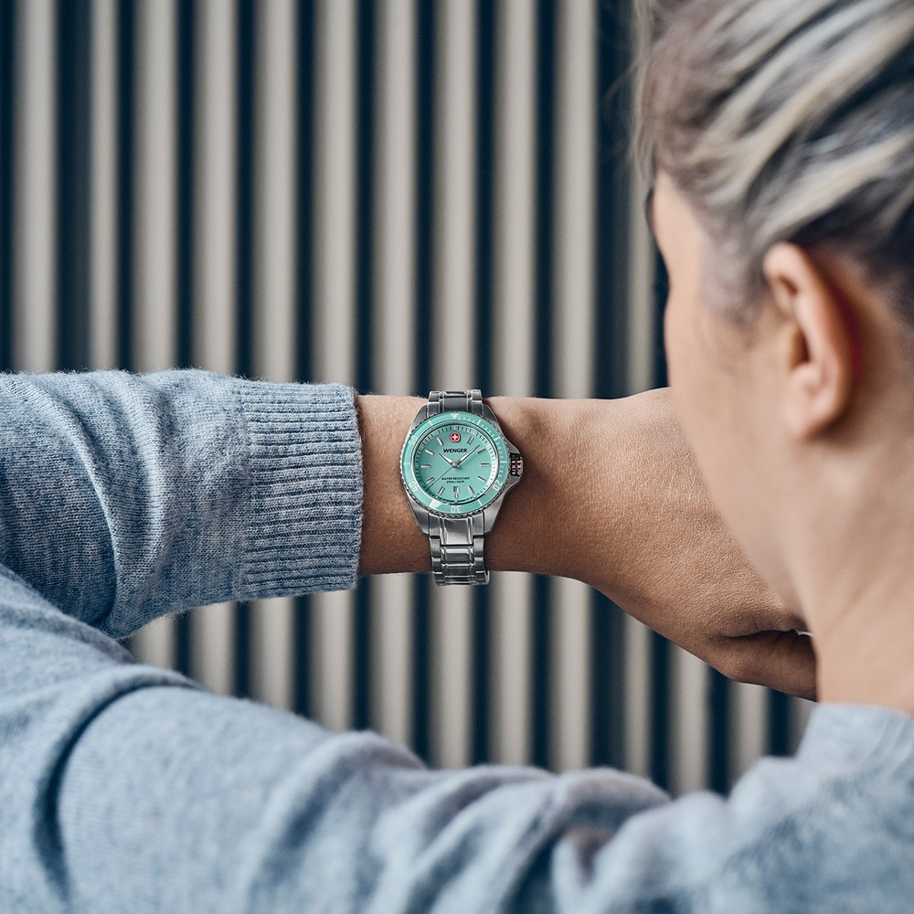 A woman looks at her mint green Wenger wristwatch on her left wrist.