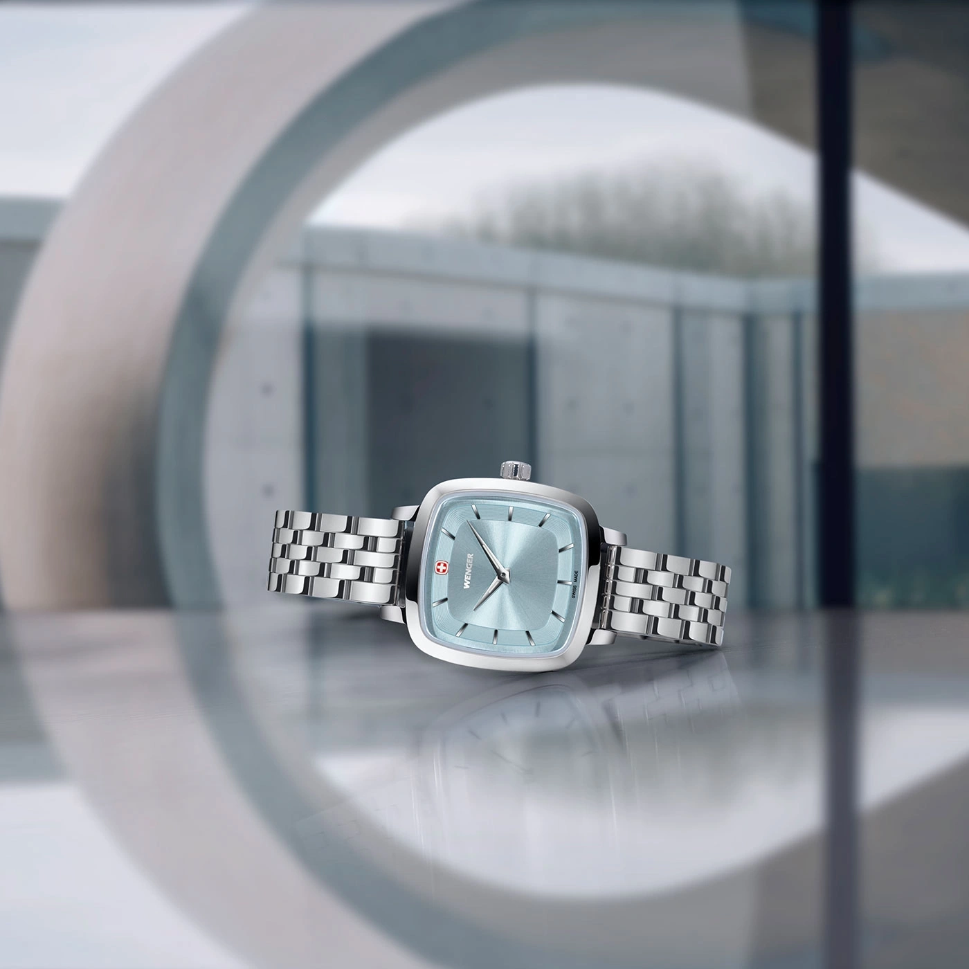 Uhr mit hellblauem Zifferblatt und silbernem Armband, vor modernem Hintergrund