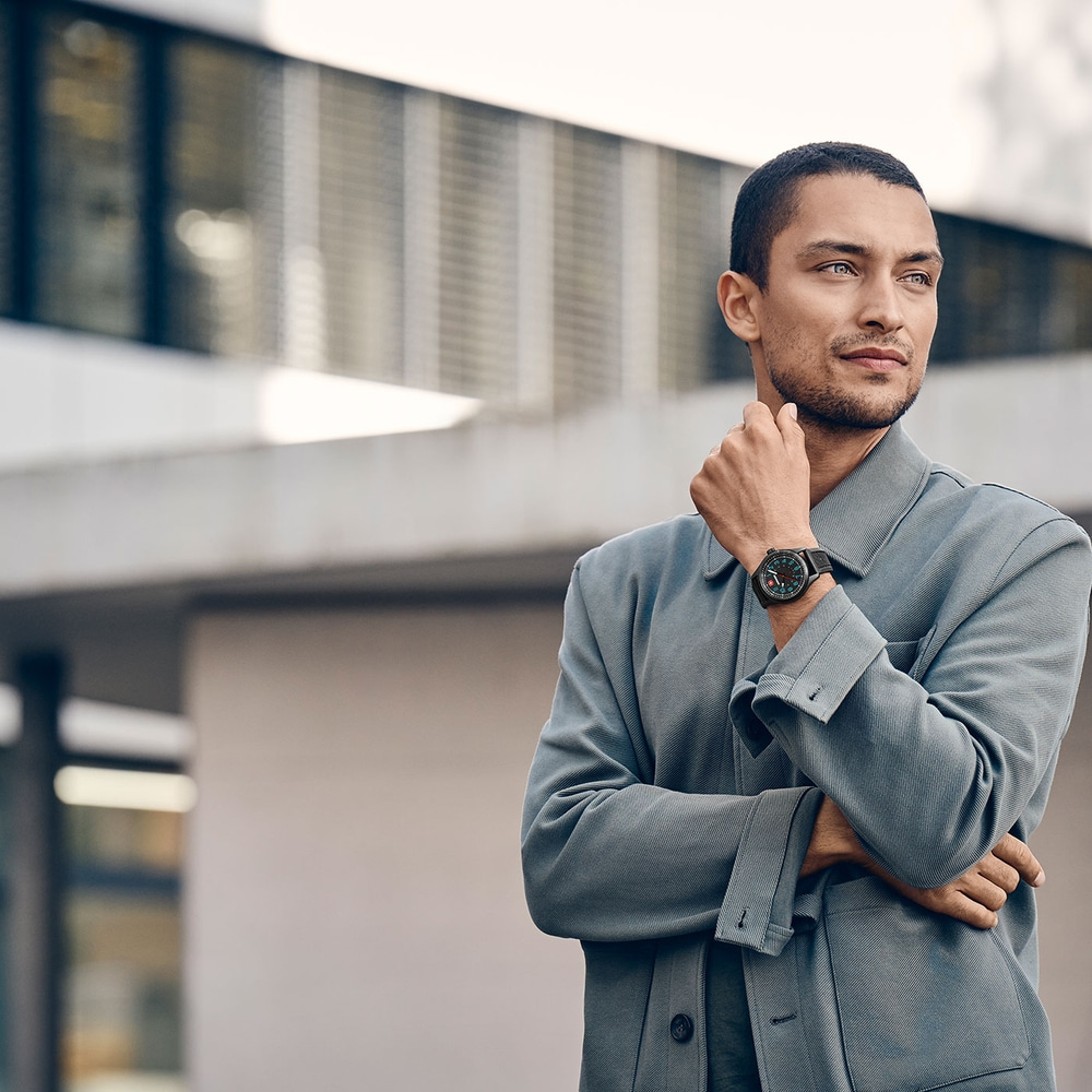 Man wearing a watch looking into the distance in front of a building