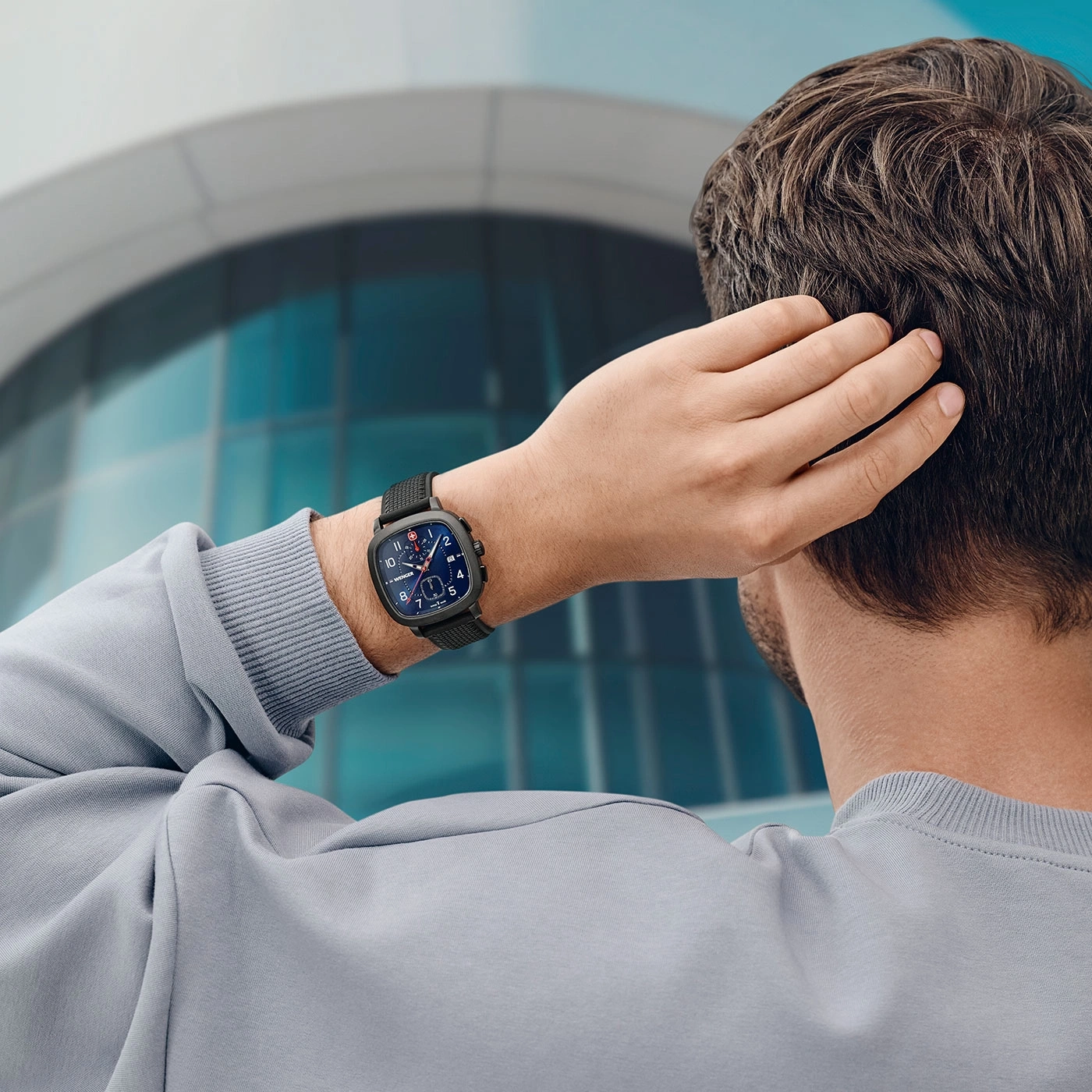Mann mit Uhr, der sich am Kopf kratzt, vor einem Gebäude