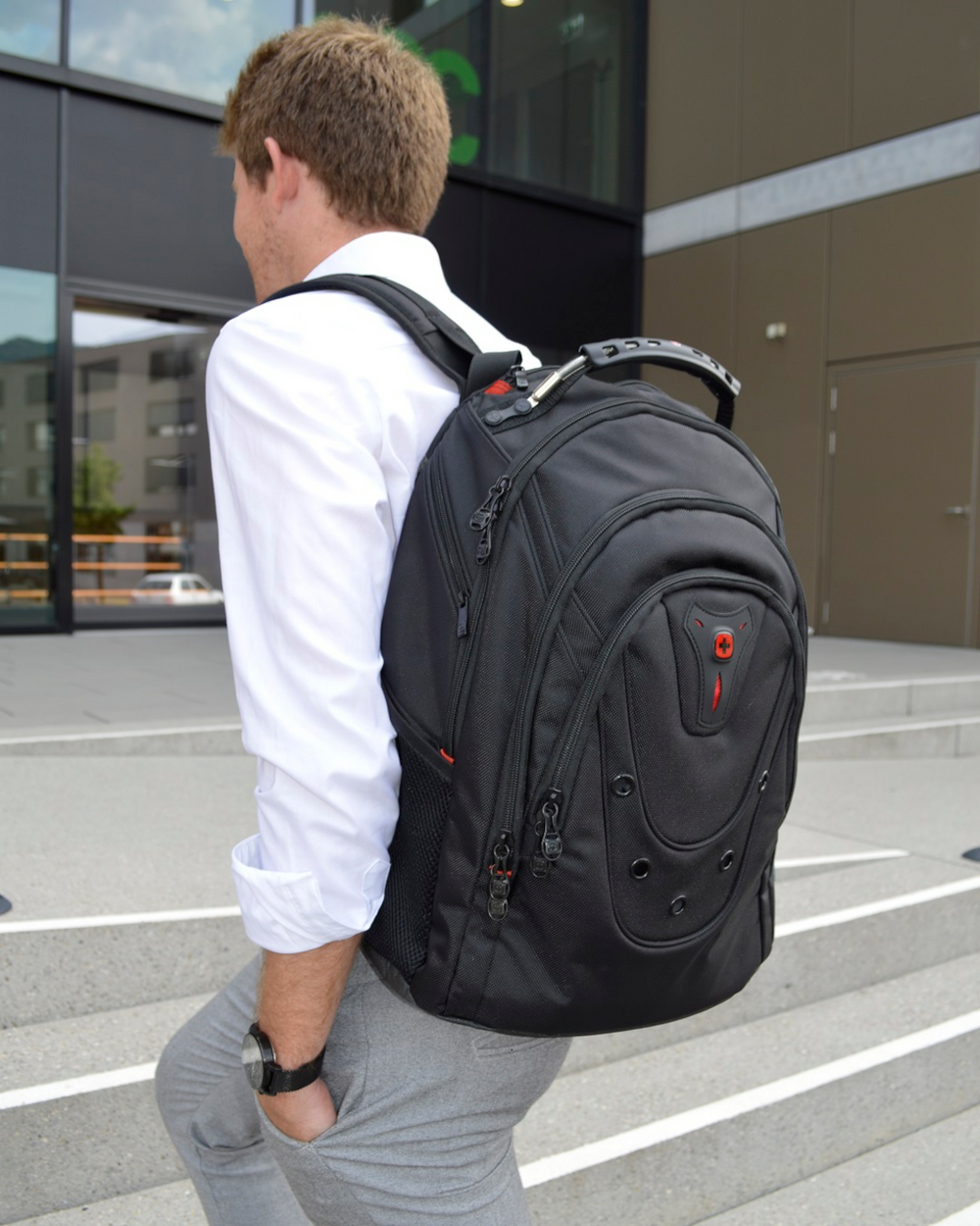 Man with black backpack walking up stairs, looking back at the camera