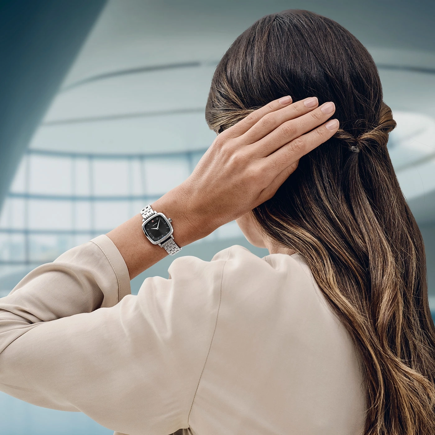 Frau mit Uhr, die sich die Haare hält, vor verschwommenem Hintergrund