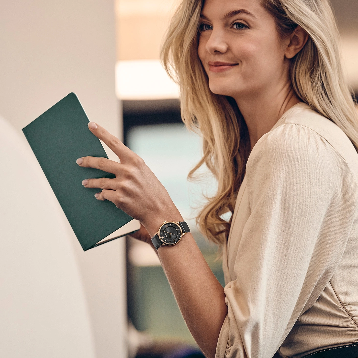Une femme aux cheveux blonds tient un livre vert dans ses mains.