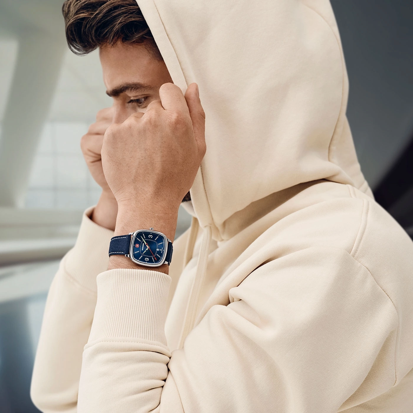 Man in hoodie with watch pulling hood over head, looking down, close up.