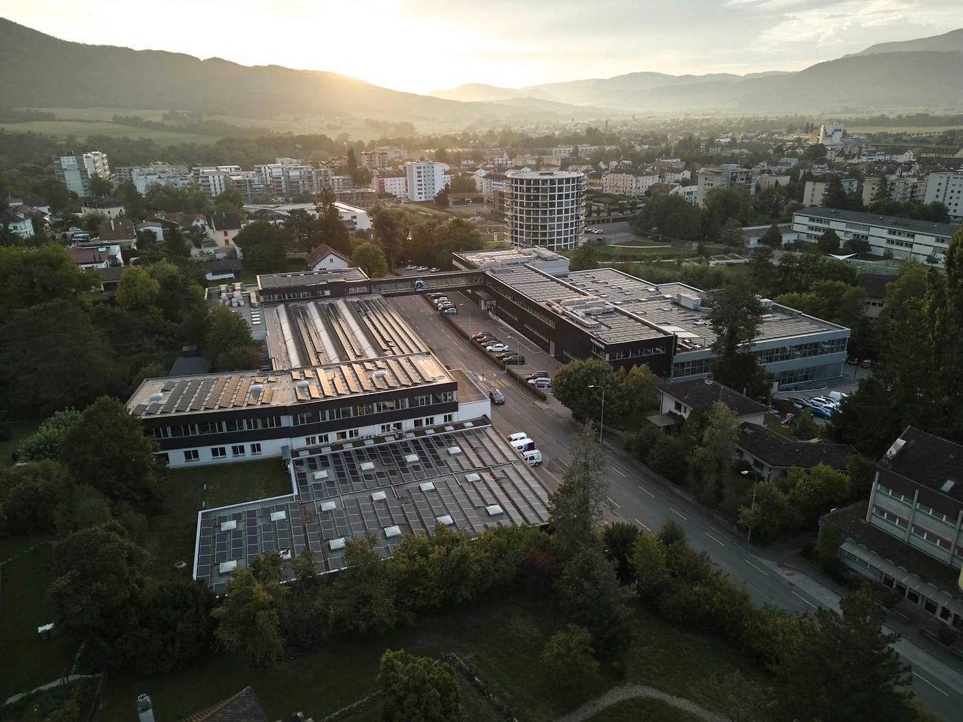 Drohnenaufnahme eines Industriegebiets mit Solaranlagen und Bergen im Hintergrund bei Sonnenuntergang.