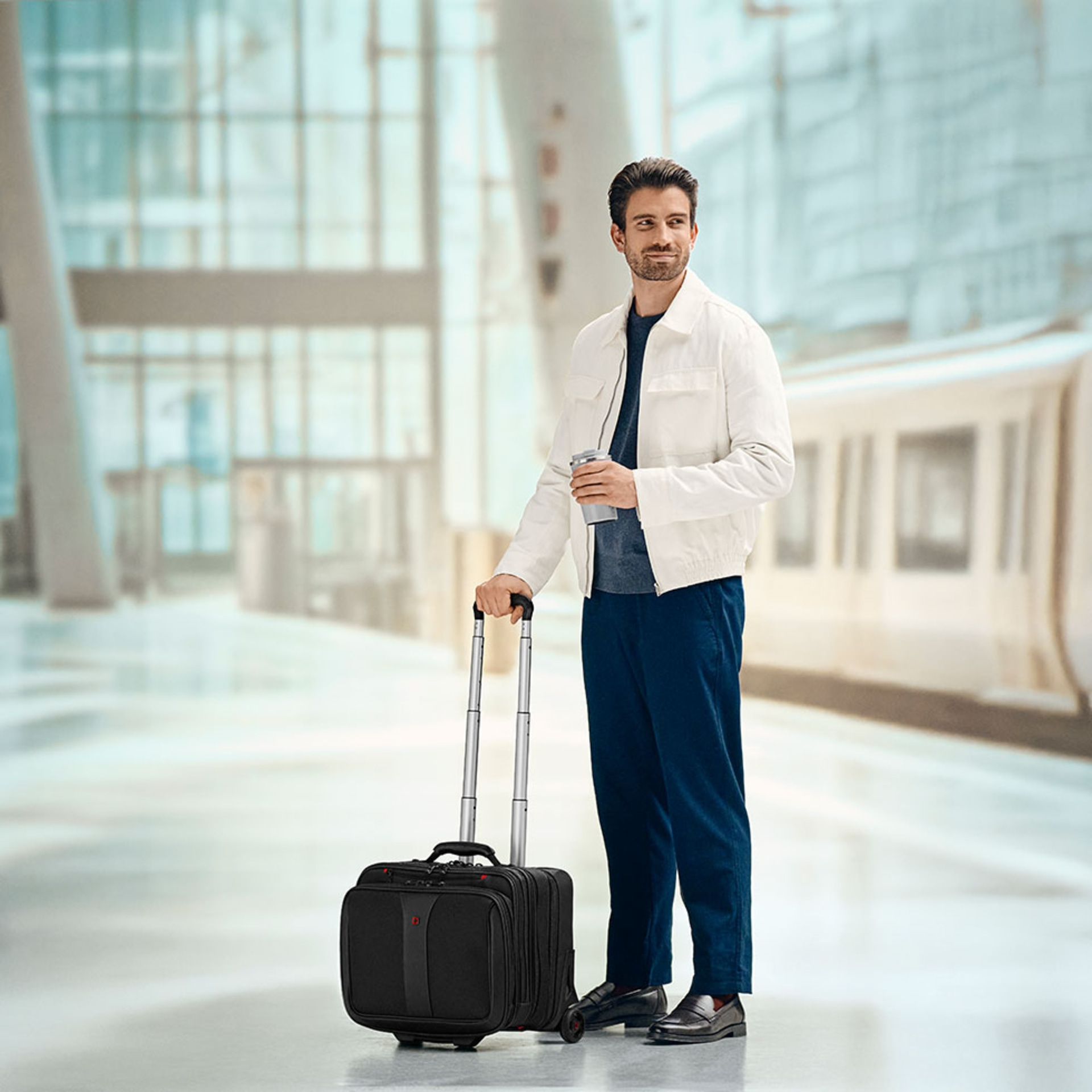 Man with suitcase and coffee waiting at the train station.