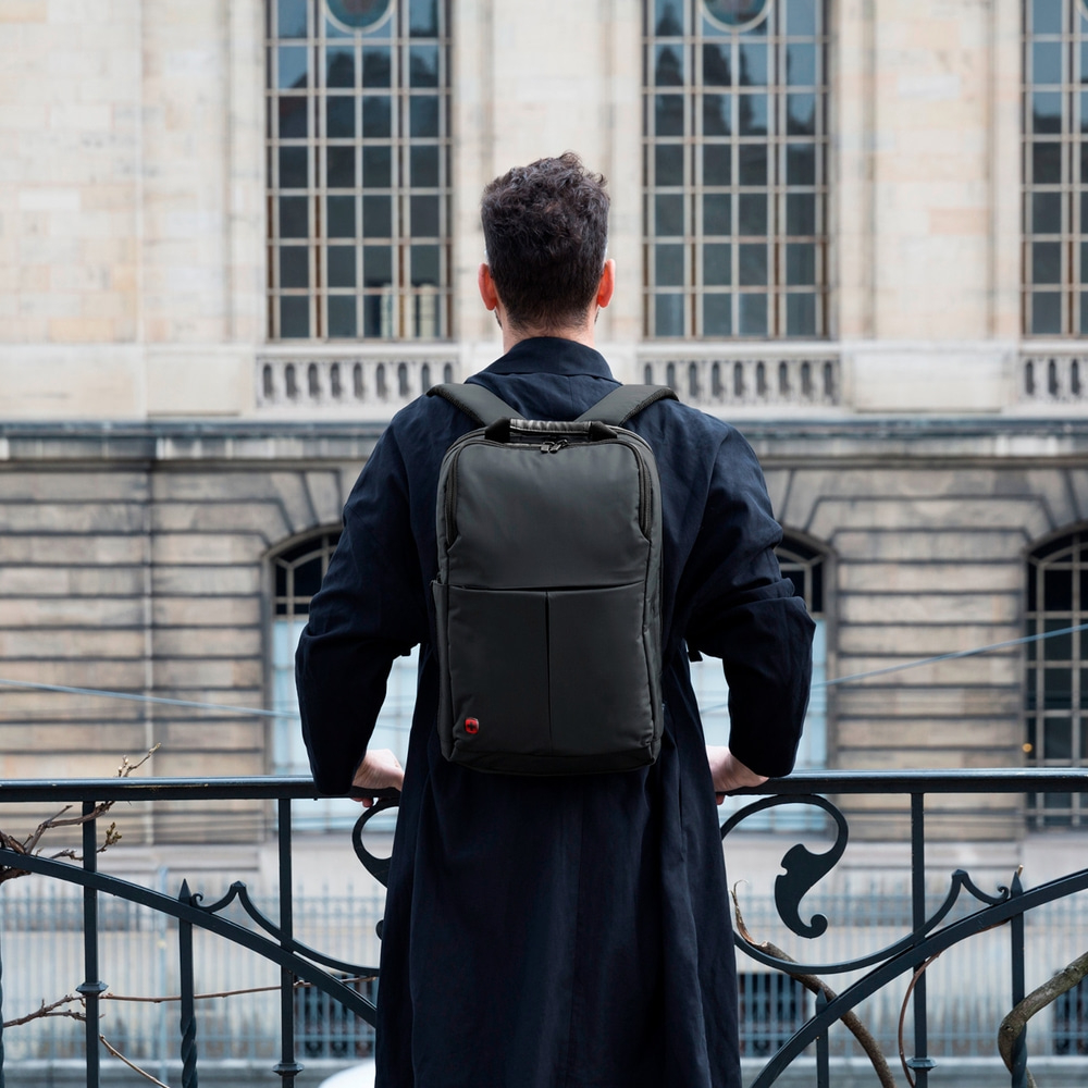 Man with backpack stands in front of a building, looking away from the camera.