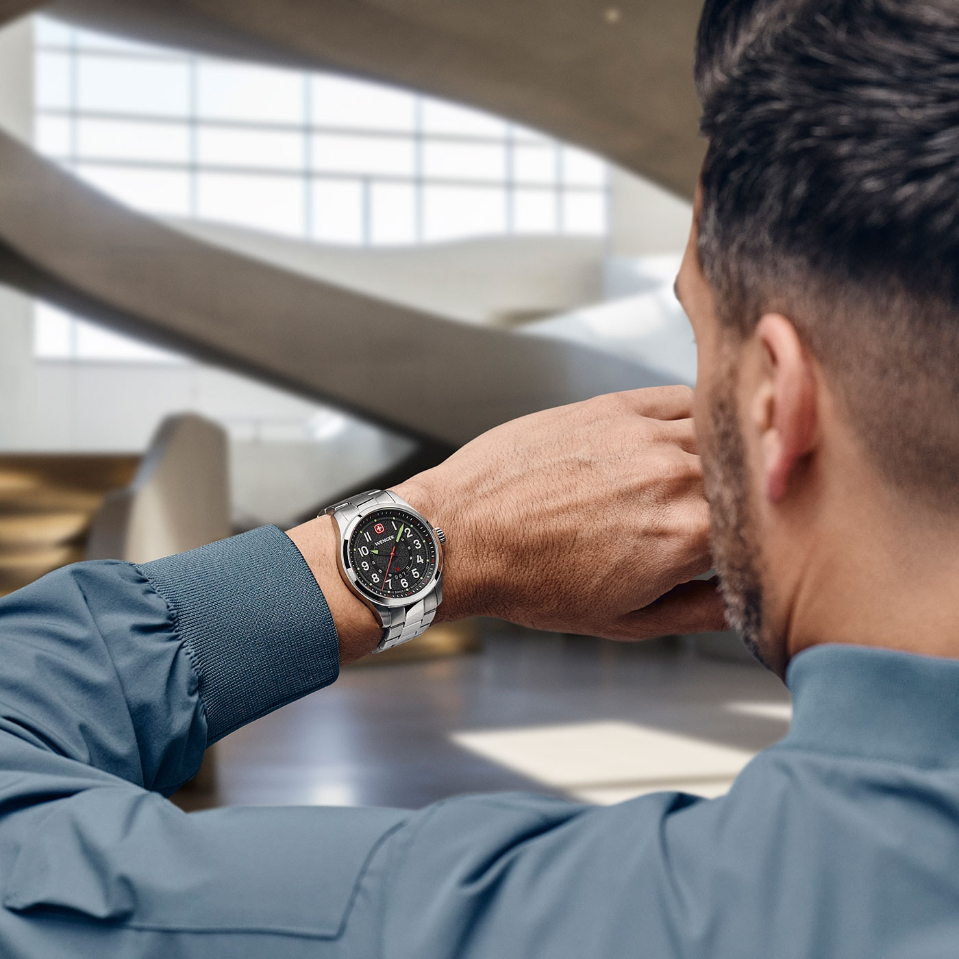 Man looking at his watch. He is wearing a blue jacket. The background is blurred.