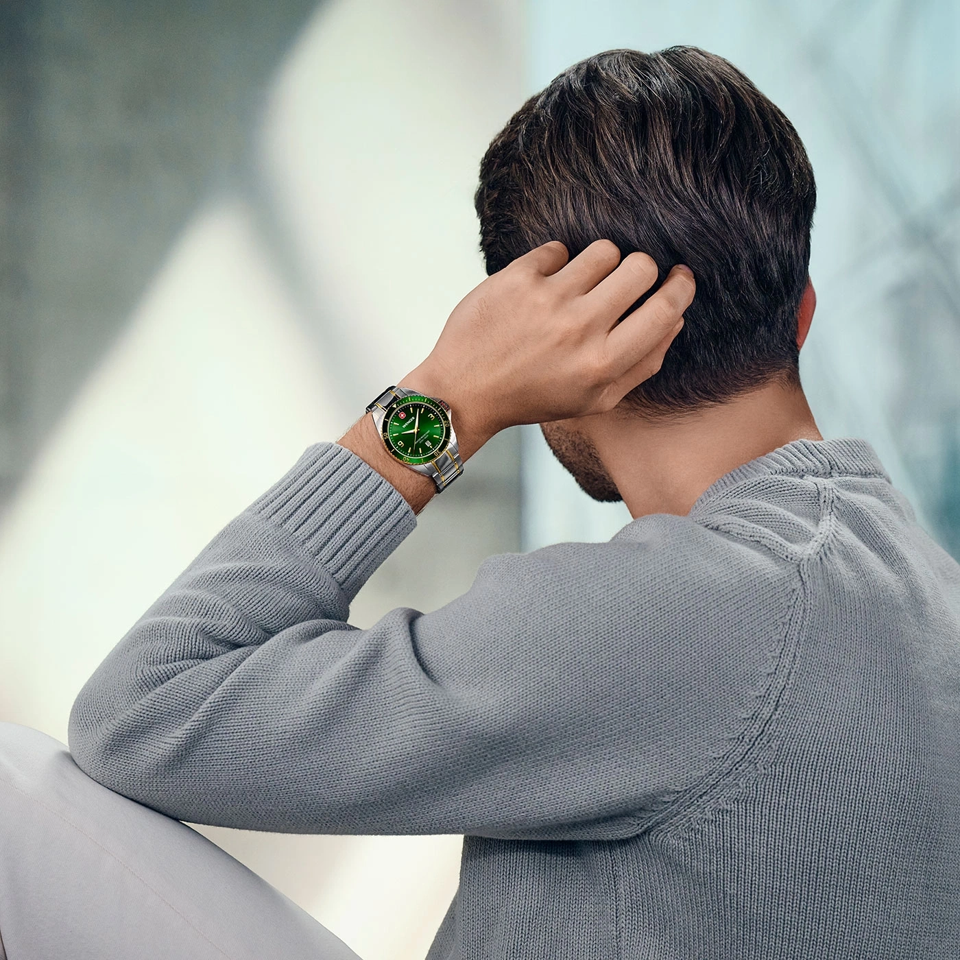 Man with watch scratching head, gray sweater, light pants, green watch face