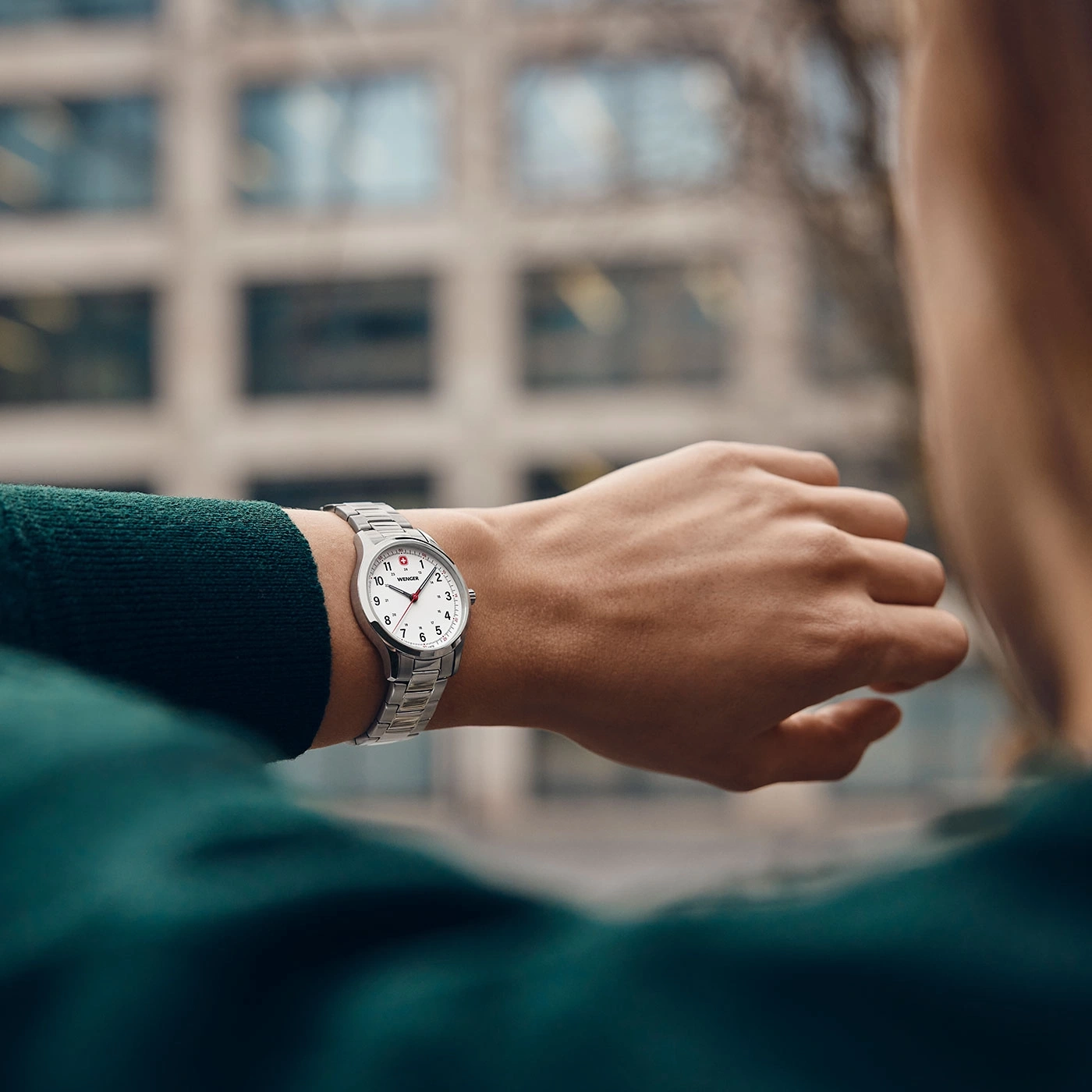 Close-up of a person wearing a silver watch on their wrist, against a blurred background