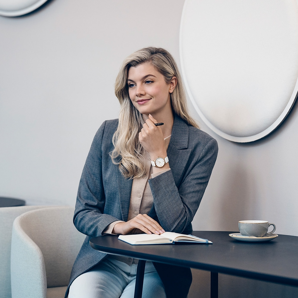 A woman with blonde hair sits at a table with a notebook and coffee cup.