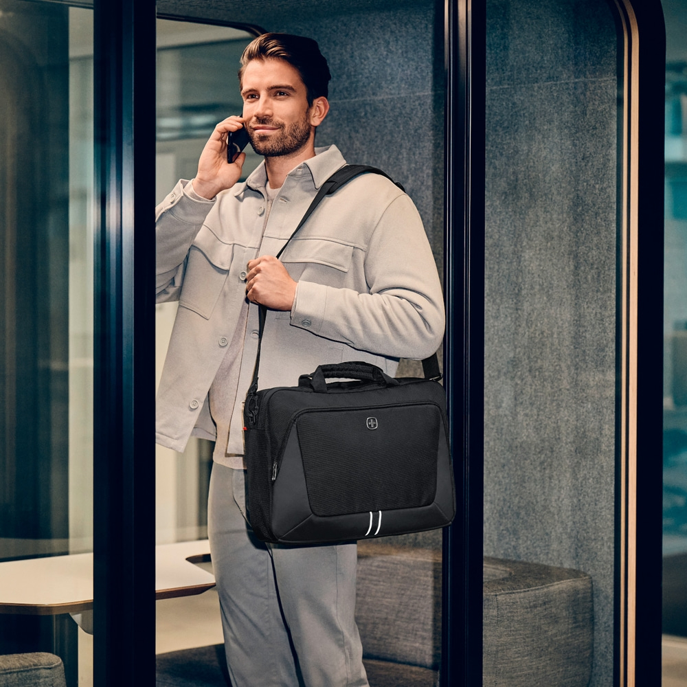 Man in office talking on phone, wearing grey clothes, carrying a black bag