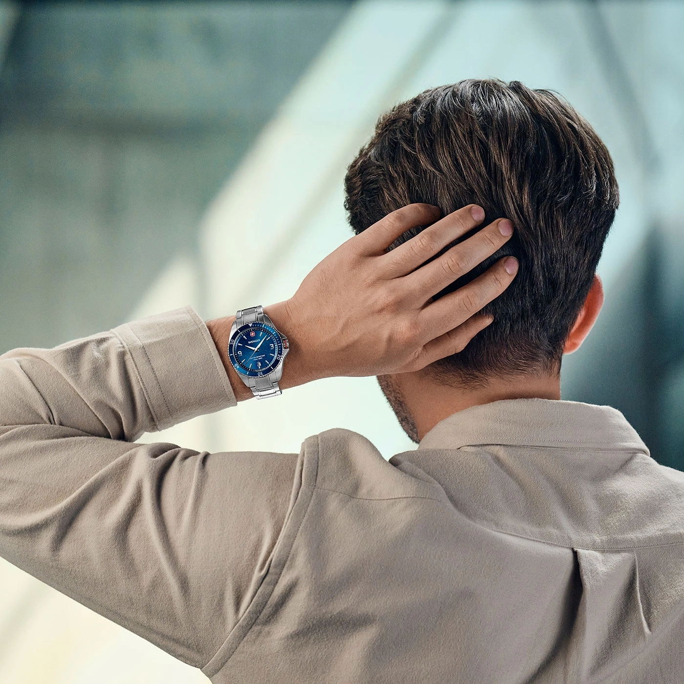 Man with watch scratching head, back view, light shirt, blue watch face