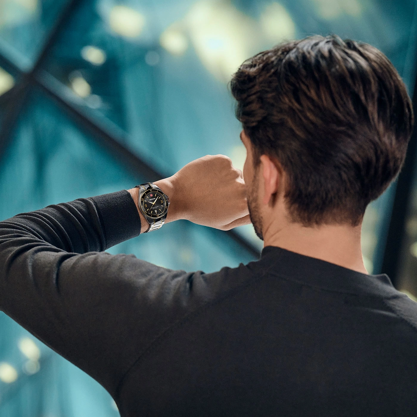 Man looking at his watch, wearing a black shirt, with a blue background