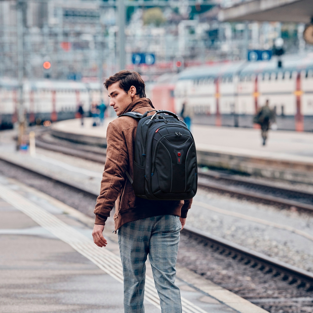 Man with backpack at train station, looking back, brown jacket, plaid pants, train