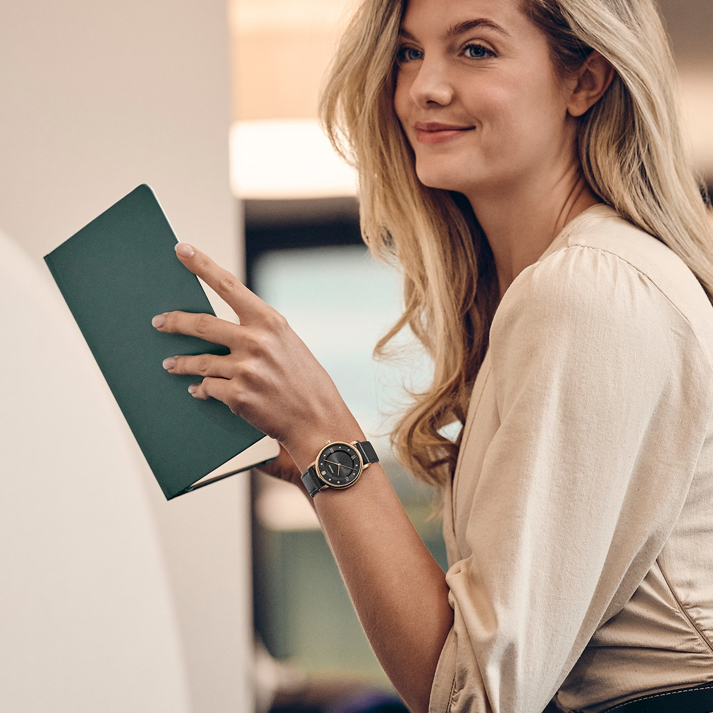 A blonde woman holds a green book in her hands.