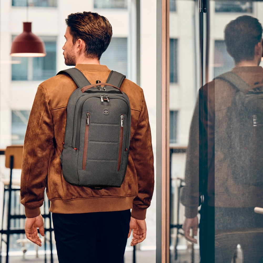 Man with backpack walking through glass door, wearing brown jacket