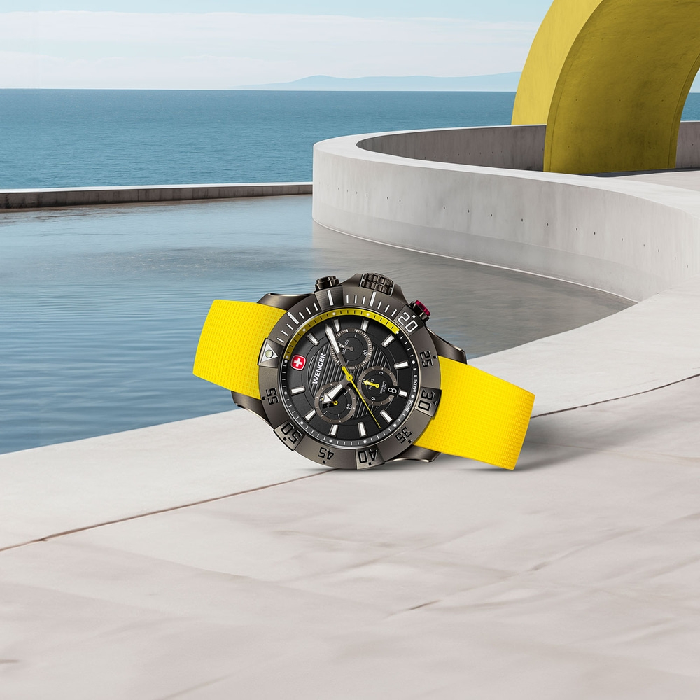 Watch with yellow strap on concrete surface with ocean view and yellow arch