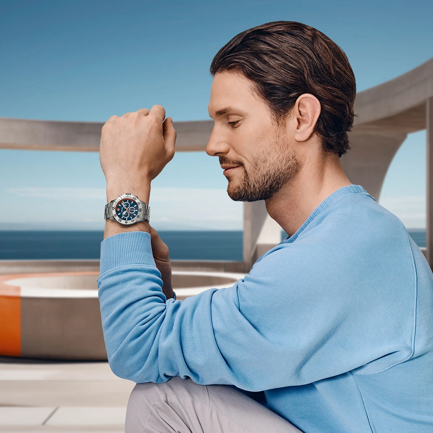 Man wearing watch, blue shirt, looking down, against blue sky and building