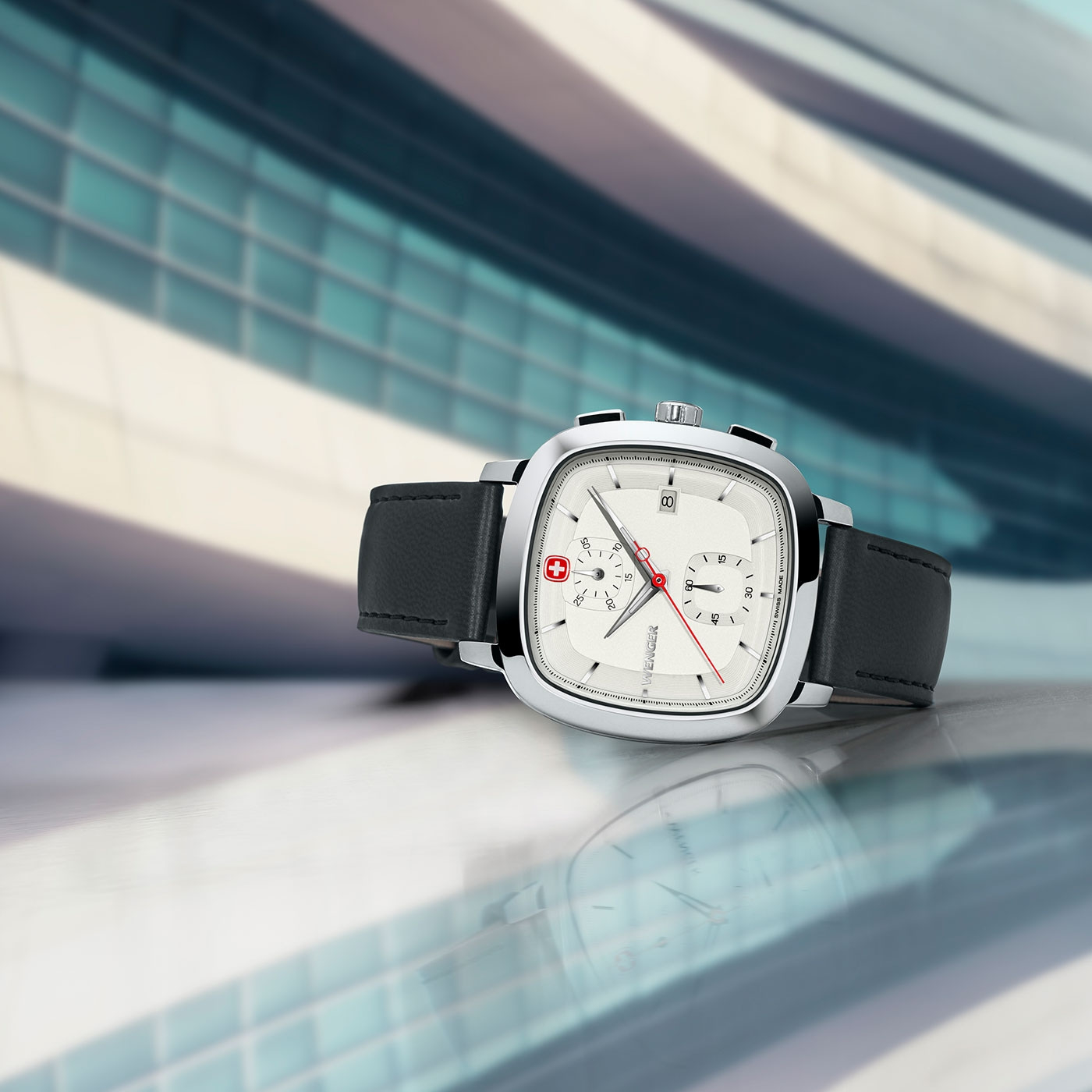 Watch with black leather strap on glossy surface in front of modern building