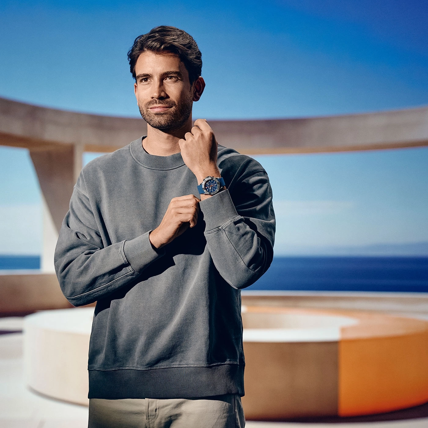 Man wearing watch, grey sweater, posing, background sea and sky, sunny