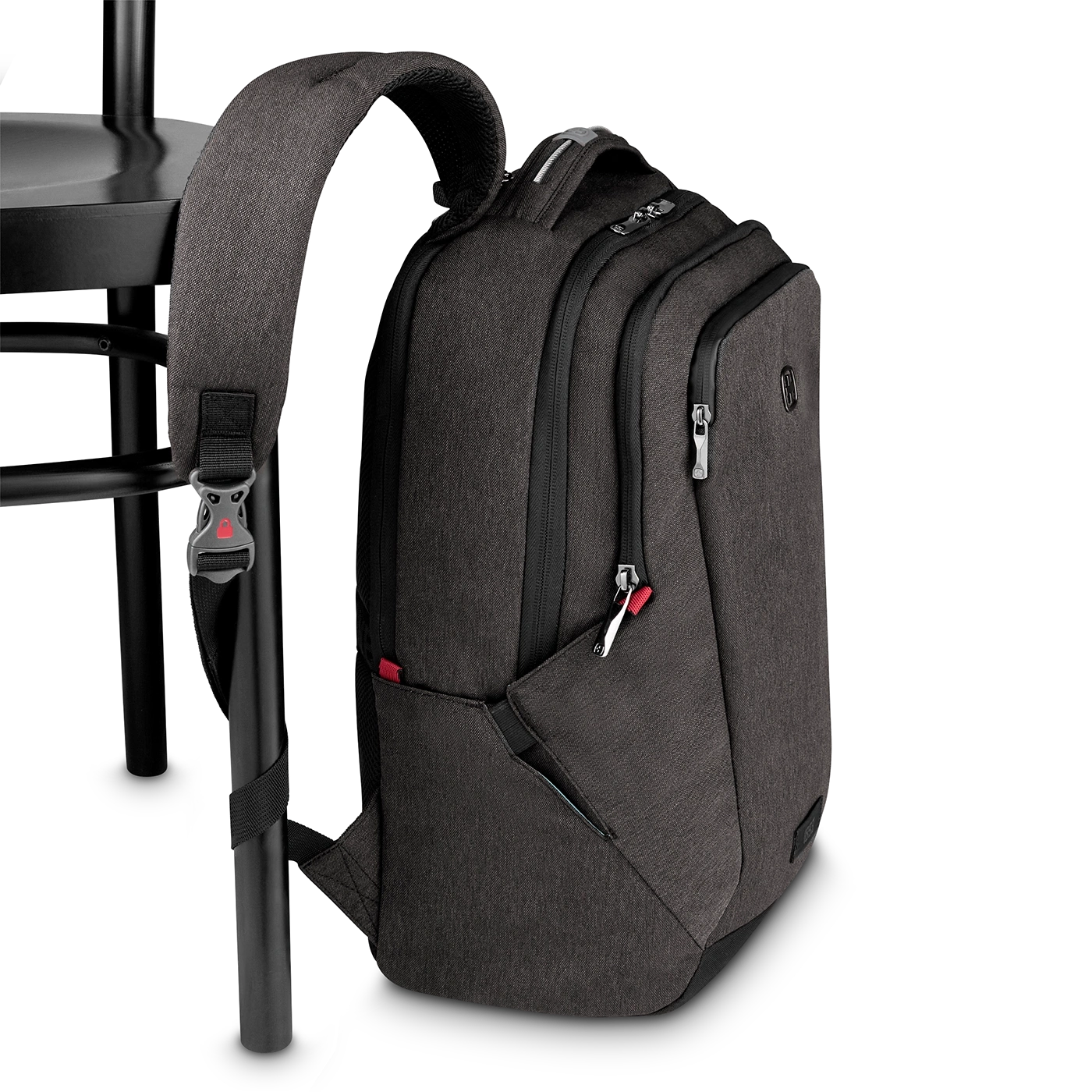 Dark gray backpack hanging on a black chair with red accents and zippers.