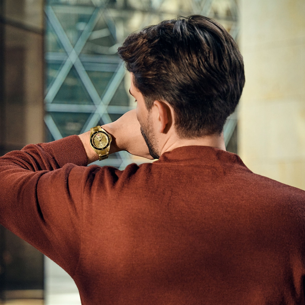 Man looking at his gold watch, wearing a red sweater, in front of a window