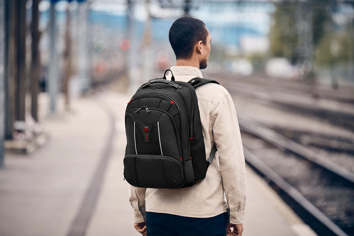 Mann mit Rucksack auf Bahnhofsplattform, Blick auf Gleise.