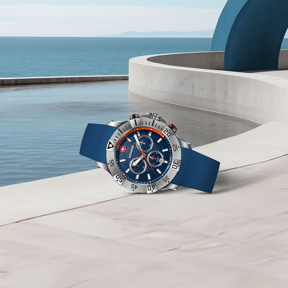 Watch with blue strap on white surface with ocean view and blue sky in the background.
