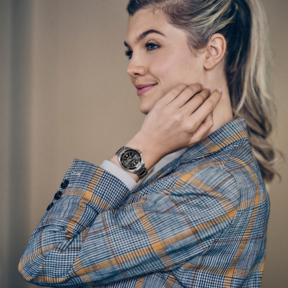 A woman with blue eyes wears a checkered blazer and a watch on her wrist.