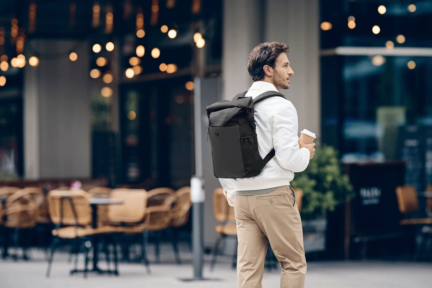 Man with backpack and coffee walks past a cafe.