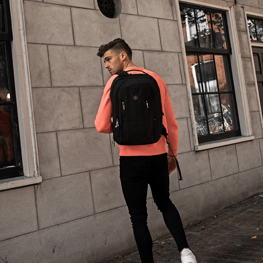 Man with backpack walking past a building, wearing black pants and white shoes
