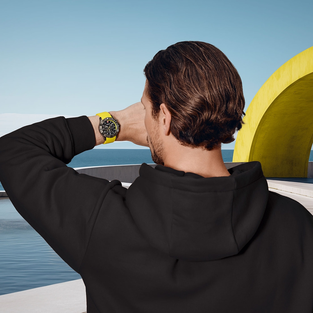 Man looking at watch, sea in background, yellow arch, black hoodie