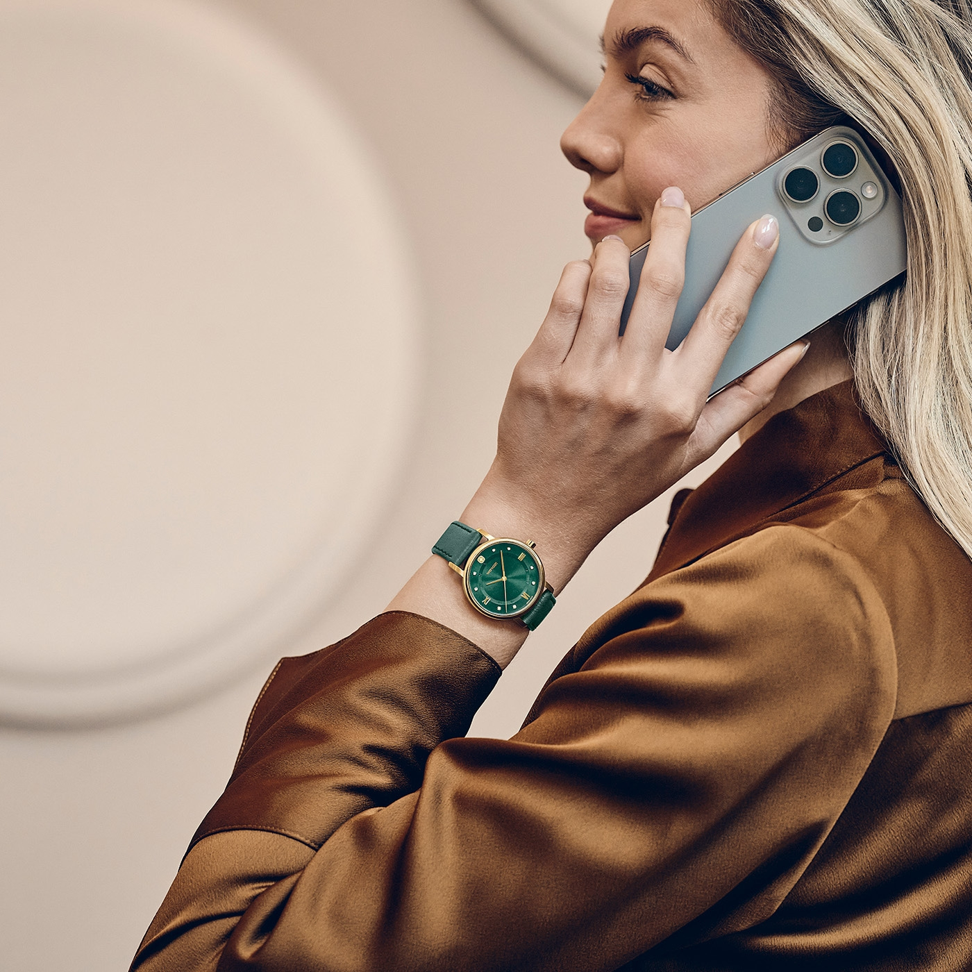 A woman talks on a smartphone while wearing a green wristwatch.