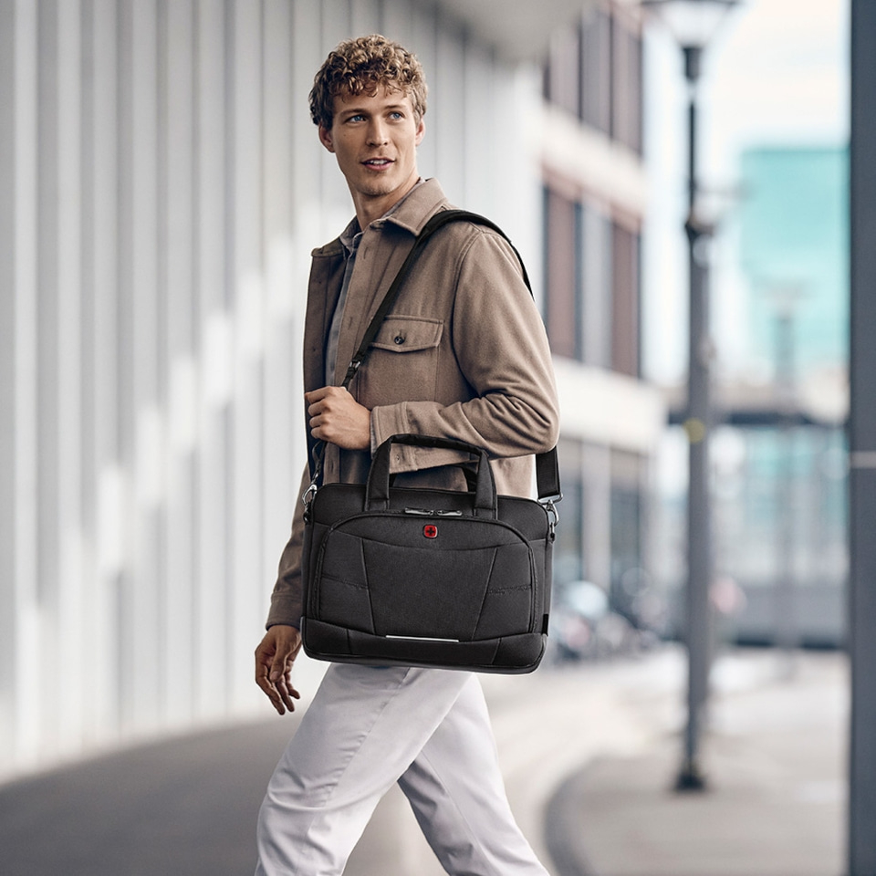 Man walking with a black bag, looking away, in front of a building, urban scene.