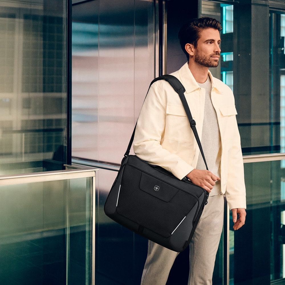 Man with black bag in front of glass facade, casual clothes, looking to the side