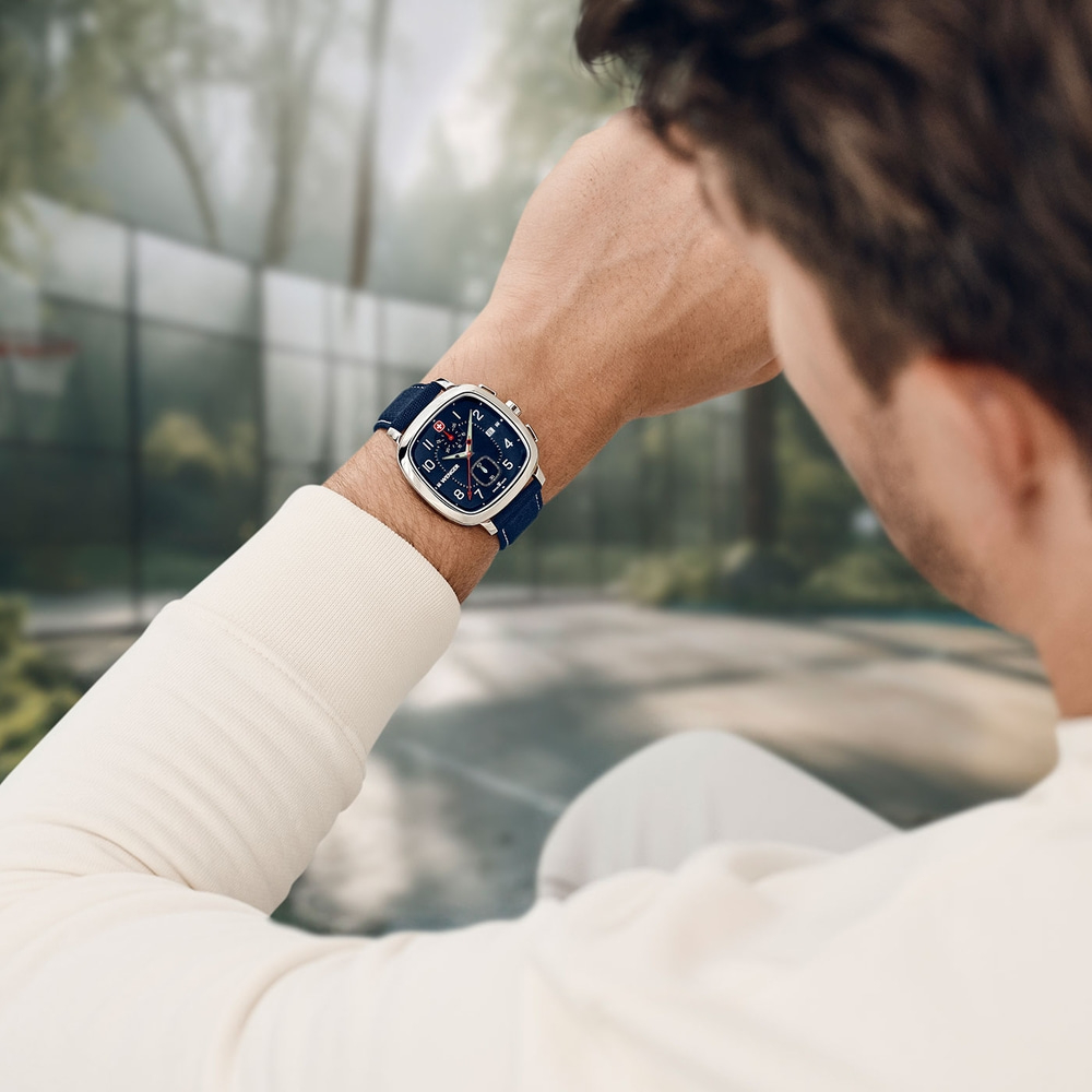 Man wearing a watch outdoors with a blurred background, looking at his wrist.