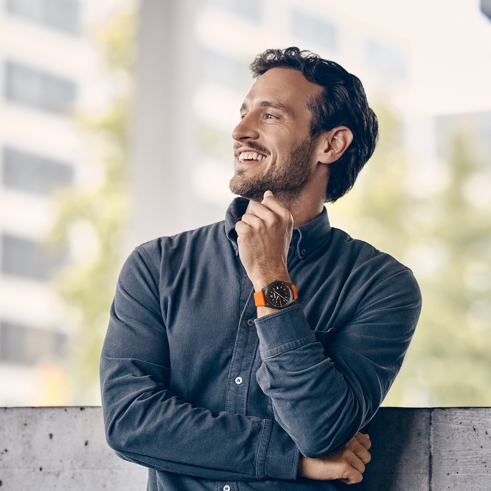 A man with a beard wearing a watch on his arm, thinking.