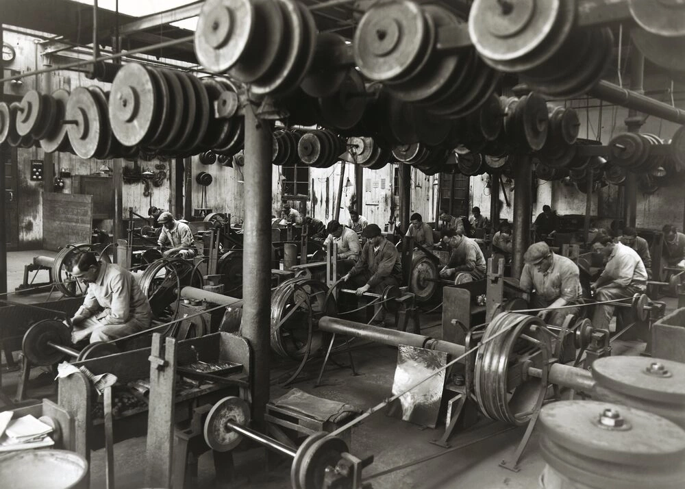 Men working at machines in a factory with many pulleys.