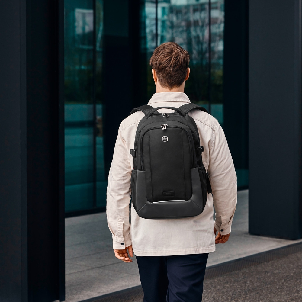 Man with black backpack walking in front of a building.