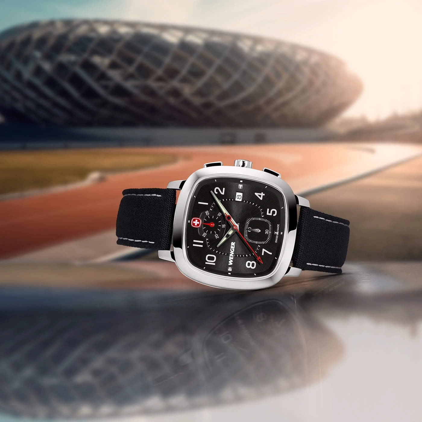 Wenger Uhr mit schwarzem Zifferblatt und Armband, vor unscharfem Stadionhintergrund.