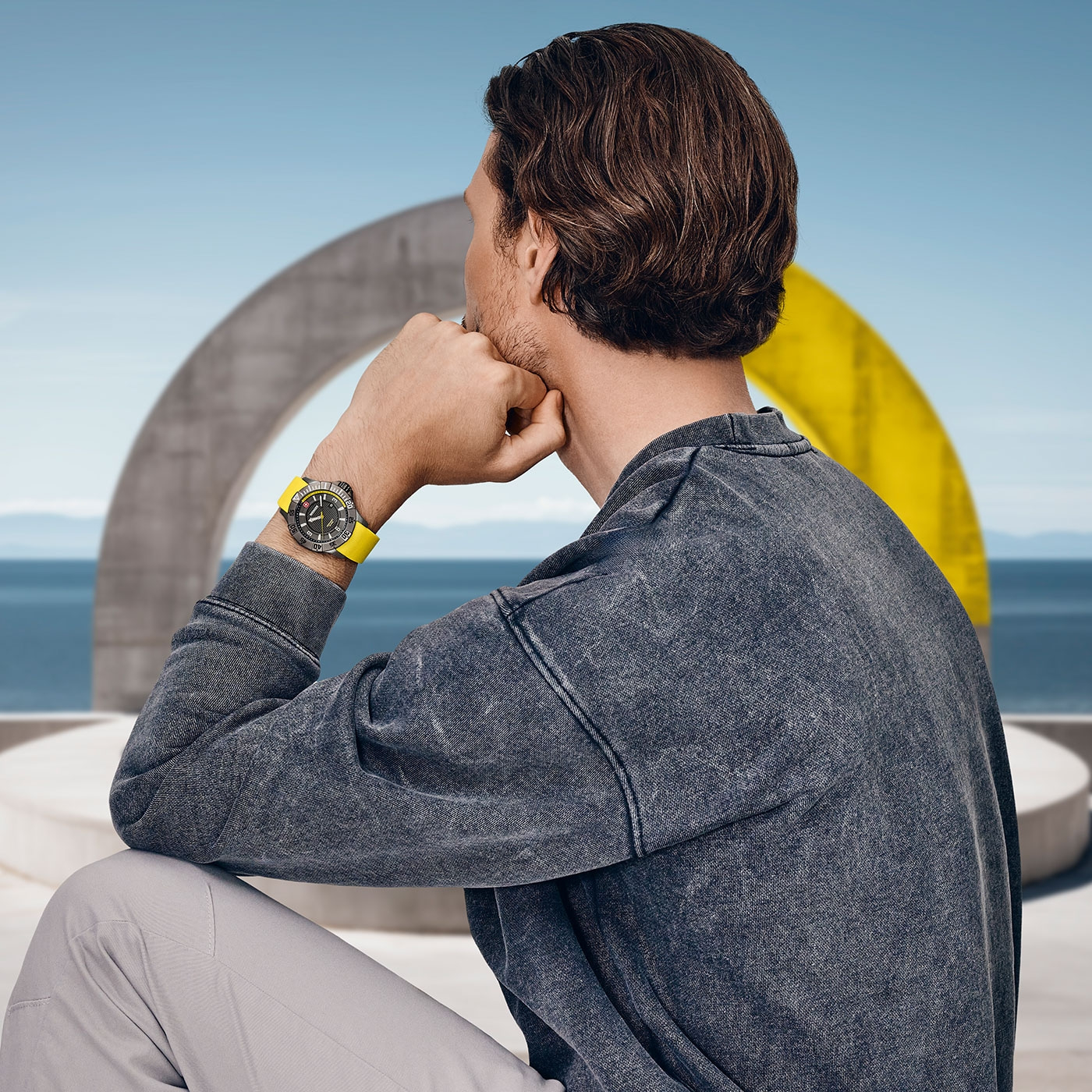 Man looking at the sea with a watch, in front of a yellow arch